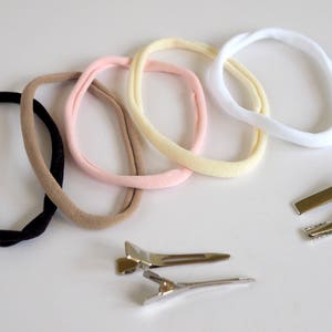 May include: Five different colored elastic hair ties in black, brown, pink, yellow, and white. Two silver metal hair clips are also included.