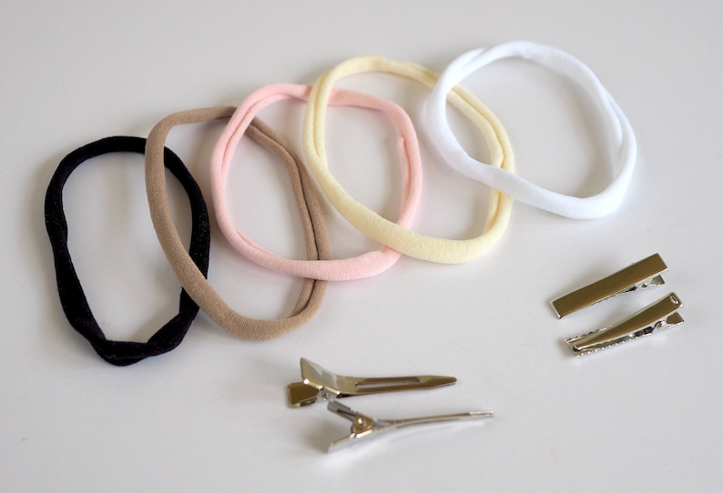 May include: Five different colored elastic hair ties in black, brown, pink, yellow, and white. Two silver metal hair clips are also included.
