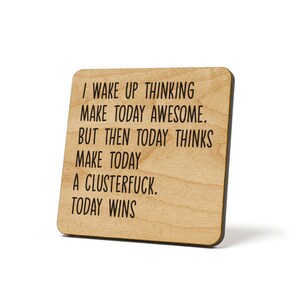 May include: Wooden coaster with a funny quote: "I wake up thinking make today awesome. But then today thinks make today a clusterfuck. Today wins."