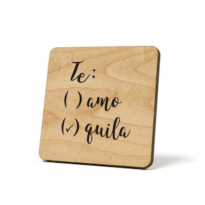 May include: A wooden sign with the text "Te: () amo () quila" written in black cursive font.