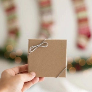 Op de afbeelding: Een bruine cadeaudoos gebonden met een grijs lint. De doos wordt vastgehouden door een hand.