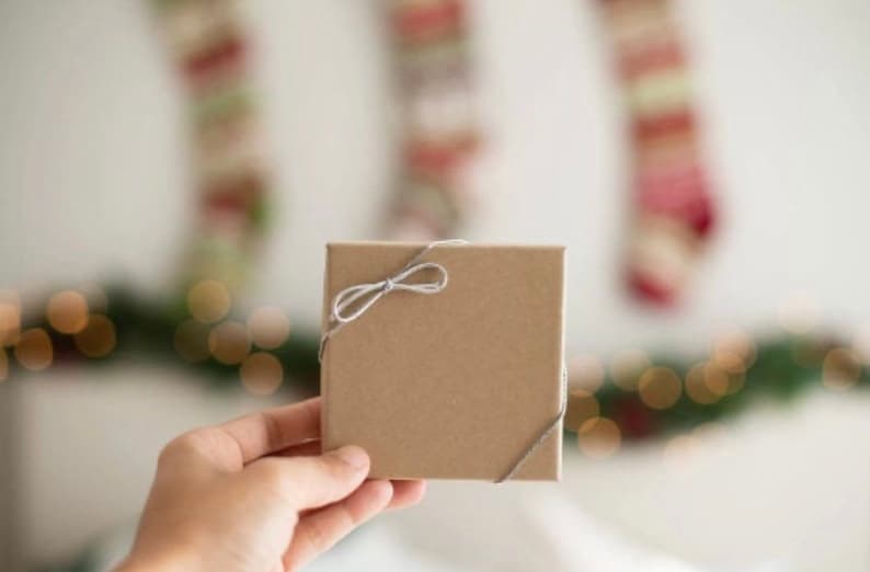 Op de afbeelding: Een bruine cadeaudoos gebonden met een grijs lint. De doos wordt vastgehouden door een hand.