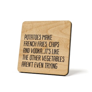 May include: A wooden square coaster with rounded corners. The coaster has a light brown wood grain finish and features black text that reads: "POTATOES MAKE FRENCH FRIES, CHIPS AND VODKA...IT'S LIKE THE OTHER VEGETABLES AREN'T EVEN TRYING."
