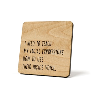 May include: Wooden coaster with the text "I need to teach my facial expressions how to use their inside voice."