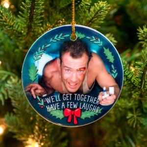 May include: A round Christmas ornament with a blue background and a holly wreath border. The ornament features a photo of a man with a bloody nose and a cigarette lighter in his hand. The text "We'll get together have a few laughs" is printed on the ornament.