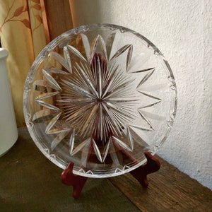 Könnte beinhalten: Eine klare Glasservierplatte mit einem Sternmuster. Die Platte steht auf einem Holzständer.