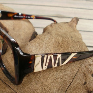 May include: Tortoise shell eyeglasses with gold accents on the arms. The arms have a geometric pattern with a gold finish.