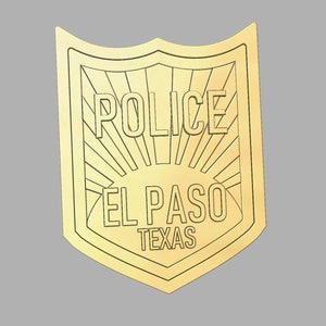 May include: A gold-colored metal police badge with the words "POLICE", "EL PASO", and "TEXAS" inscribed on it. The badge has a sunburst design.