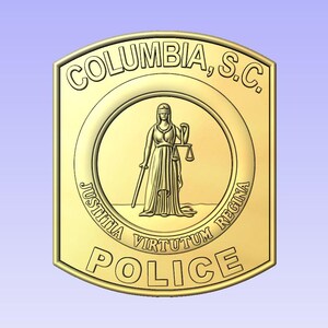 May include: A gold-colored police badge with the words "COLUMBIA, S.C." at the top. The center features a figure holding scales and a sword, with the words "JUSTITIA VIRTUTUM REGINA" and "POLICE" below.