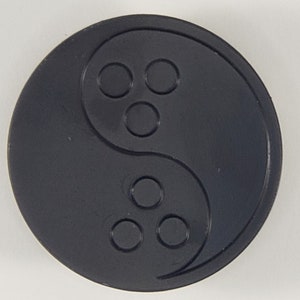 May include: A black circular disc with a yin yang symbol in the center. The yin yang symbol is made up of two halves, one black and one white, with a small circle of the opposite color in each half. There are three small circles on each side of the yin yang symbol.