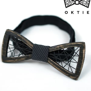 Puede incluir: Una pajarita de madera negra con un diseño de cuerda negra. La pajarita está unida a una banda elástica negra.