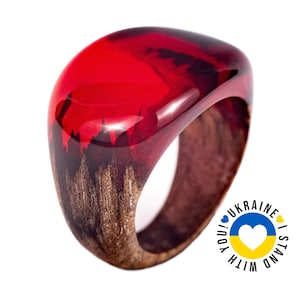 May include: A red and brown resin ring with a unique design. The ring is made of wood and resin and has a glossy finish. The ring is a statement piece and would be a great addition to any jewellery collection.