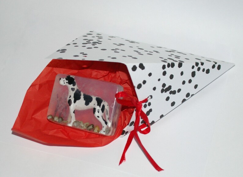 Puede incluir: Una figurita de perro d&aacute;lmata blanco y negro dentro de una bolsa de regalo blanca con cinta roja y papel de seda rojo.