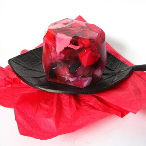 Könnte beinhalten: Ein roter, rosa und schwarzer geometrischer Seifenblock auf einer schwarzen, blattartigen Schale. Die Schale befindet sich auf einem roten Seidenpapier.