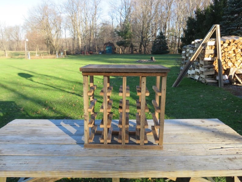 Puede incluir: Un estante de vino de madera r&uacute;stico con forma cuadrada y varios estantes. El estante est&aacute; hecho de madera reciclada y tiene un acabado natural. Est&aacute; sentado en una mesa de madera.