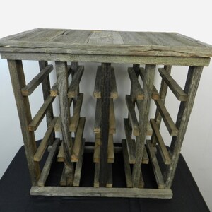 Puede incluir: Un estante de vino de madera r&uacute;stico con un acabado gris desgastado. El estante tiene varios estantes para guardar botellas de vino.