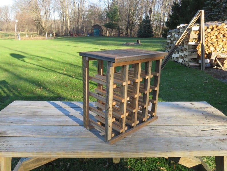 Puede incluir: Un estante de vino de madera r&uacute;stico con un acabado natural. El estante tiene m&uacute;ltiples ranuras para guardar botellas de vino. Est&aacute; sentado en una mesa de madera.