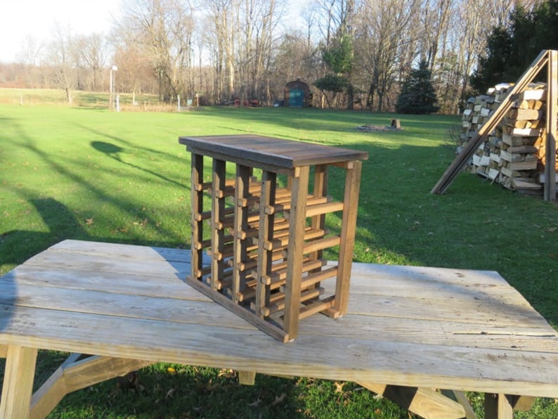 Puede incluir: Un estante de vino de madera con un acabado marr&oacute;n oscuro. El estante est&aacute; hecho de listones de madera y tiene una forma rectangular. Est&aacute; sentado en una mesa de madera.