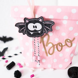May include: Pink gift bag with white polka dots and a black bat with white teeth hanging from the top. The bag says "Boo" in gold letters.