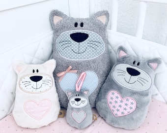 May include: Four plush cat toys in different sizes. The largest cat is gray with a white face and a pink heart. The next largest cat is white with a pink heart. The smallest cat is gray with a pink and white heart. The cats are all smiling.