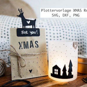 Könnte beinhalten: Eine braune Papiertüte mit einer schwarzen Rentier-Silhouette, einem schwarzen Etikett mit der Aufschrift "Für dich!" und dem Wort "XMAS" darauf gedruckt. Die Tüte ist mit Schnur gebunden und hat ein kleines Herz darauf gezeichnet. Im Hintergrund steht ein weißer Kerzenhalter mit einer schwarzen Silhouette eines Hauses und zweier Bäume.