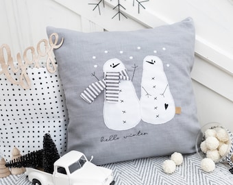 May include: Gray linen pillow with two embroidered snowmen and the text "hello winter".
