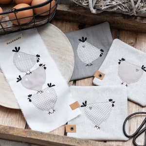 Puede incluir: Posavasos de tela blanca hechos a mano con pollos bordados grises. Los posavasos presentan un patrón a cuadros gris y blanco y el texto "Handmade".