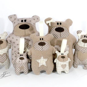 Può includere: Una collezione di ornamenti a forma di orso fatti a mano di varie dimensioni. Gli orsi sono principalmente beige e marroni, con motivi a stella, pois e quadretti. Ogni orso ha un nastro per appenderlo e un cuore o una stella.