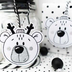 Può includere: Addobbi in feltro bianco e nero a forma di orsi con corna di renna. Gli addobbi sono appesi a un barattolo di vetro e a una borsa regalo a pois bianchi e neri.