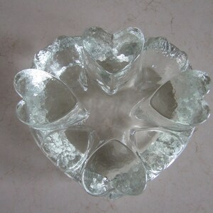 May include: A clear glass bowl with a heart-shaped design. The bowl is made of thick glass and has a textured surface.