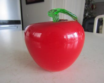 May include: A glossy red glass apple-shaped decorative item with a green stem. The apple has a smooth, reflective surface, and the stem curves gracefully. This unique piece could be used as a decorative bowl or a whimsical accent.