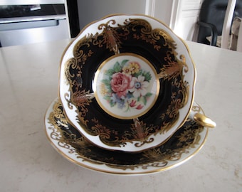 May include: A black and white teacup and saucer set with gold trim and a floral design. The teacup has a black interior and a white exterior with a gold rim. The saucer has a white exterior with a black interior and a gold rim.