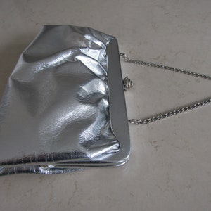 Cartera de mano plateada con asa de cadena.