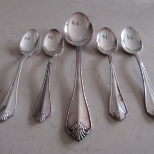 Peut inclure: Cinq cuillères en argent avec des manches ornés. Les cuillères sont disposées en rangée, la plus grande cuillère au centre.