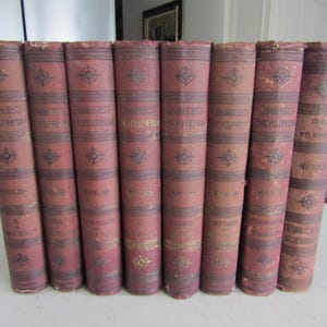 May include: A collection of antique books with burgundy covers. The spines display the title "CHAMBERS'S ENCYCLOPEDIA" in gold lettering, along with volume numbers. Decorative gold accents and patterns adorn the covers, suggesting a vintage aesthetic.