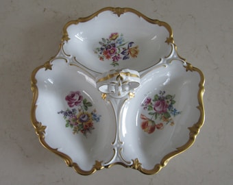 May include: A white porcelain serving dish with three sections and a gold handle. The dish is decorated with floral patterns in shades of pink, yellow, and blue.