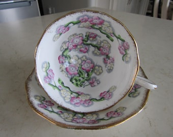 May include: A vintage teacup and saucer set with a floral design. The cup and saucer are white with a gold trim and feature a delicate pattern of pink and white flowers with green leaves.