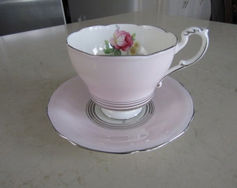 May include: A pink teacup and saucer set with a floral design. The cup has a silver rim and a silver band around the bottom. The saucer has a silver rim.
