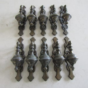 Peut inclure: Ensemble de dix boutons de cabinet en laiton antique avec des motifs ornés. Chaque bouton présente un dessus rond et bulbeux décoratif et une base longue et étroite avec une extrémité pointue.