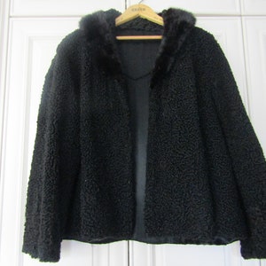 May include: A black fur coat with a fur collar. The coat is hanging on a wooden hanger.
