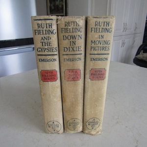 May include: Three vintage paperback books with the title "Ruth Fielding" on the spine. The books are titled "Ruth Fielding and the Gypsies", "Ruth Fielding Down in Dixie", and "Ruth Fielding in Moving Pictures".
