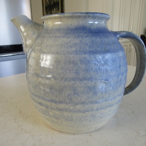 May include: A blue and white ceramic teapot with a rounded body and a handle. The teapot has a glazed finish and a subtle striped pattern.