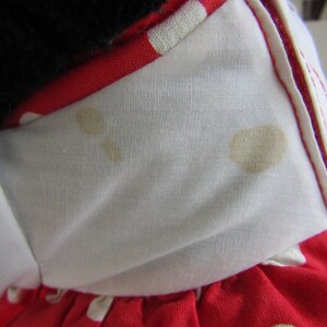May include: Close-up of a red and white polka dot dress with a white collar. The collar has brown stains. The dress is made of a soft fabric and has a white bow.