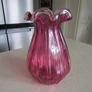 May include: A pink glass vase with a ruffled top and a ribbed design.