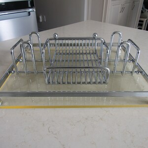 May include: A chrome-plated dish rack with a clear glass base and a chrome-plated wire rack. The rack has four compartments for utensils and a central compartment for dishes.
