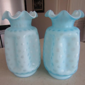 May include: Two light blue glass vases with a white polka dot pattern and ruffled tops.
