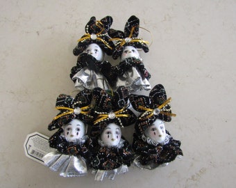 May include: Six porcelain doll ornaments with black and gold fabric costumes and silver trim. Each doll has a white face with painted features and a black bow on their head.