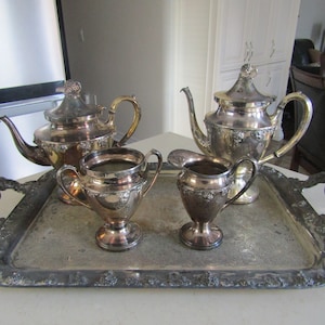 Peut inclure: Un service à thé en argent composé d'une théière, d'un pot à crème, d'un sucrier et d'un plateau. L'ensemble présente un design orné avec des motifs floraux.
