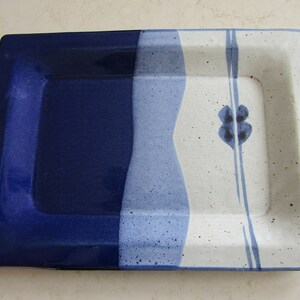 May include: A rectangular ceramic serving dish with a blue and white glaze. The dish has a raised rim and a simple floral design.