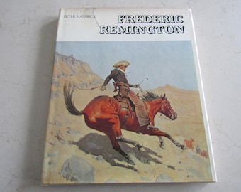 Könnte beinhalten: Buchcover mit einem Gemälde eines Cowboys auf einem braunen Pferd, das einen Hang hinunterreitet. Der Titel lautet "Frederic Remington" mit "Peter Hassrick" darüber. Der Hintergrund zeigt eine Wüstenlandschaft.